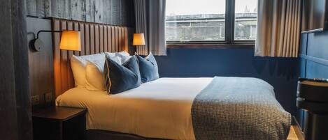 A hotel room with a bed, bedside lamps, a window with curtains, and a view of a bridge.