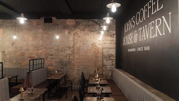A cozy interior of John's Coffee House & Tavern with exposed brick walls, wooden tables, and hanging pendant lights.