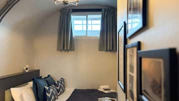 A hotel room with a bed, a nightstand, a window with curtains, and a chandelier.