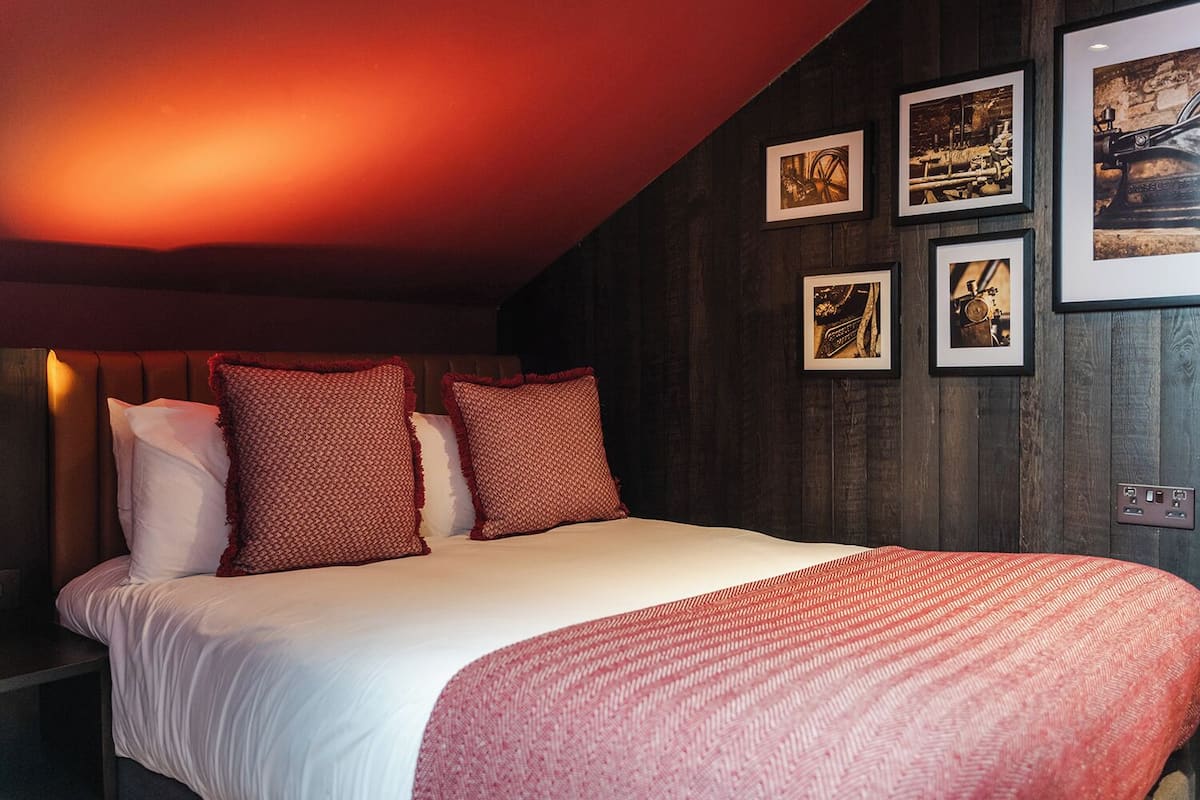A bedroom with a bed, pillows, a blanket, and framed pictures on the wall.