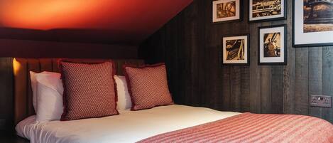A bedroom with a bed, pillows, a blanket, and framed pictures on the wall.