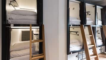 Un dormitorio estilo residencia estudiantil con literas, escaleras de madera y una ventana pequeña con un diseño de celosía.
