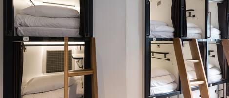 Une chambre de type dortoir, avec des lits superposés, des échelles en bois et une petite fenêtre à carreaux.