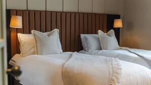 A hotel room with two beds, each with white linens and pillows, a brown headboard, and two bedside lamps.