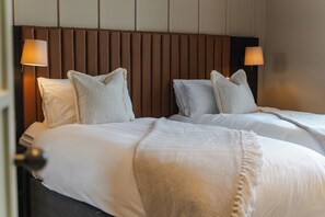 A hotel room with two beds, each with white linens and pillows, a brown headboard, and two bedside lamps.