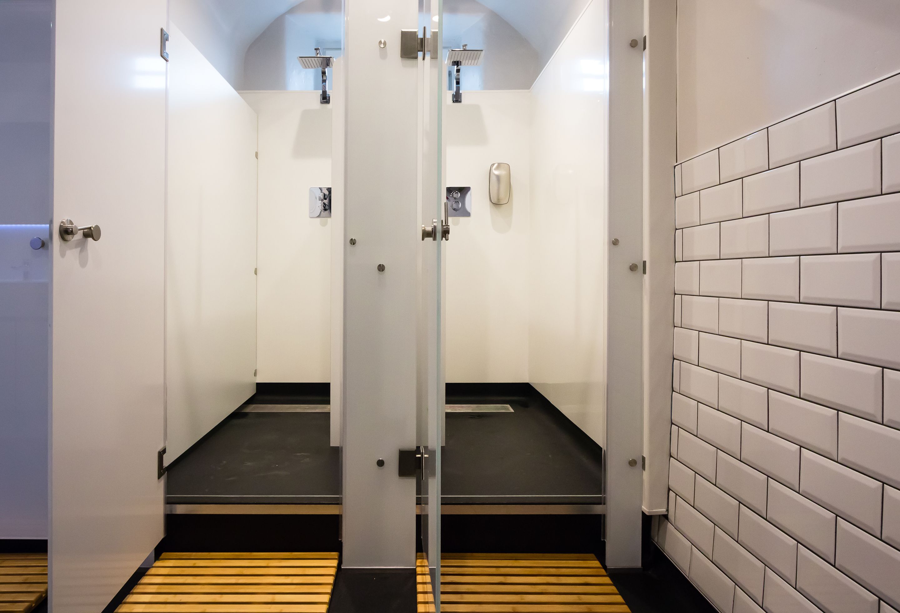 Ett modernt badrum med två duschkabiner med glasväggar, vita kakelväggar och ett trägolv.