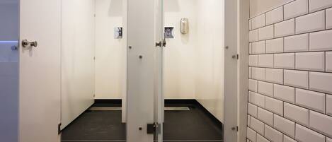 A modern bathroom with two glass-enclosed shower stalls, white tiled walls, and a wooden floor.