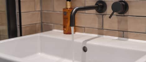Un lavamanos de baño con un grifo moderno y una botella de jabón al fondo.