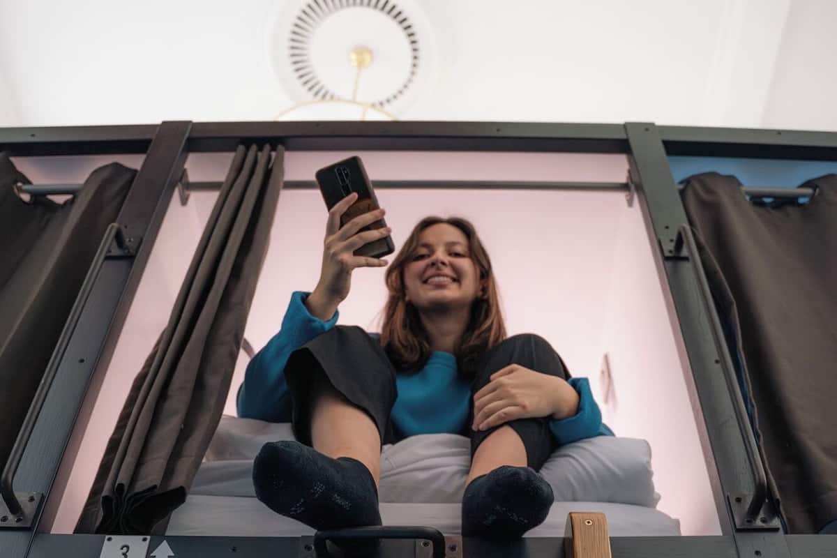 A person sitting on a bed with a ladder, holding a phone.
