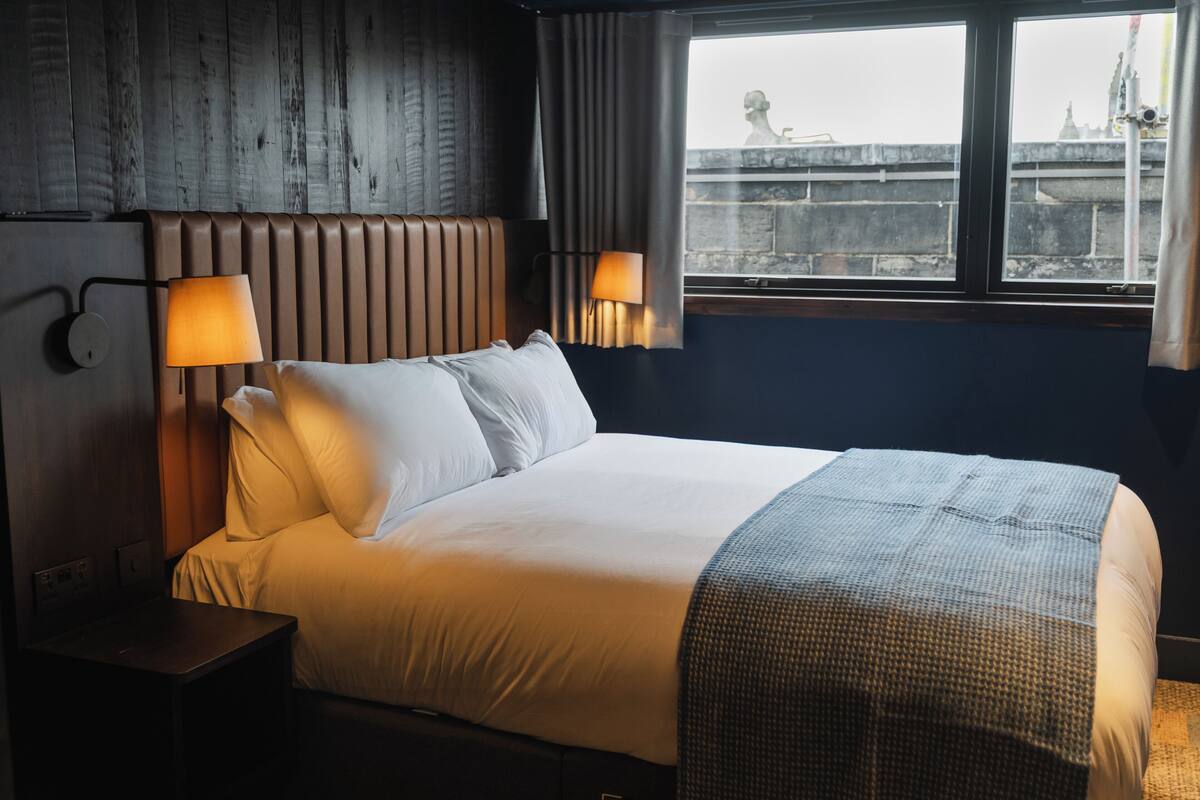 A hotel room with a large bed, two bedside lamps, a view of a bridge, and a wooden wall.
