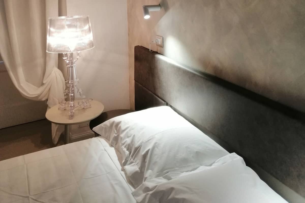 Una habitación de hotel con una cama, una mesita de noche con lámpara, y una lámpara fijada a la pared.