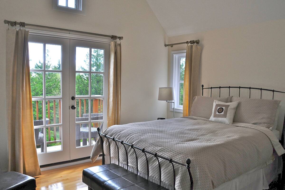 A bedroom with a large bed, a nightstand, a lamp, and a view through a sliding glass door to an outdoor area.