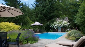 A backyard with a swimming pool, outdoor furniture, and lush greenery. - Wetherly Inn (Salt Spring Island)