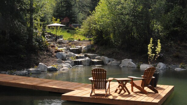 A wooden dock with two chairs and a table by a calm pond, surrounded by rocks and greenery. - Wetherly Inn (Salt Spring Island)