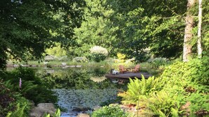 A serene garden with a pond, surrounded by lush greenery and flowering plants. - Wetherly Inn (Salt Spring Island)