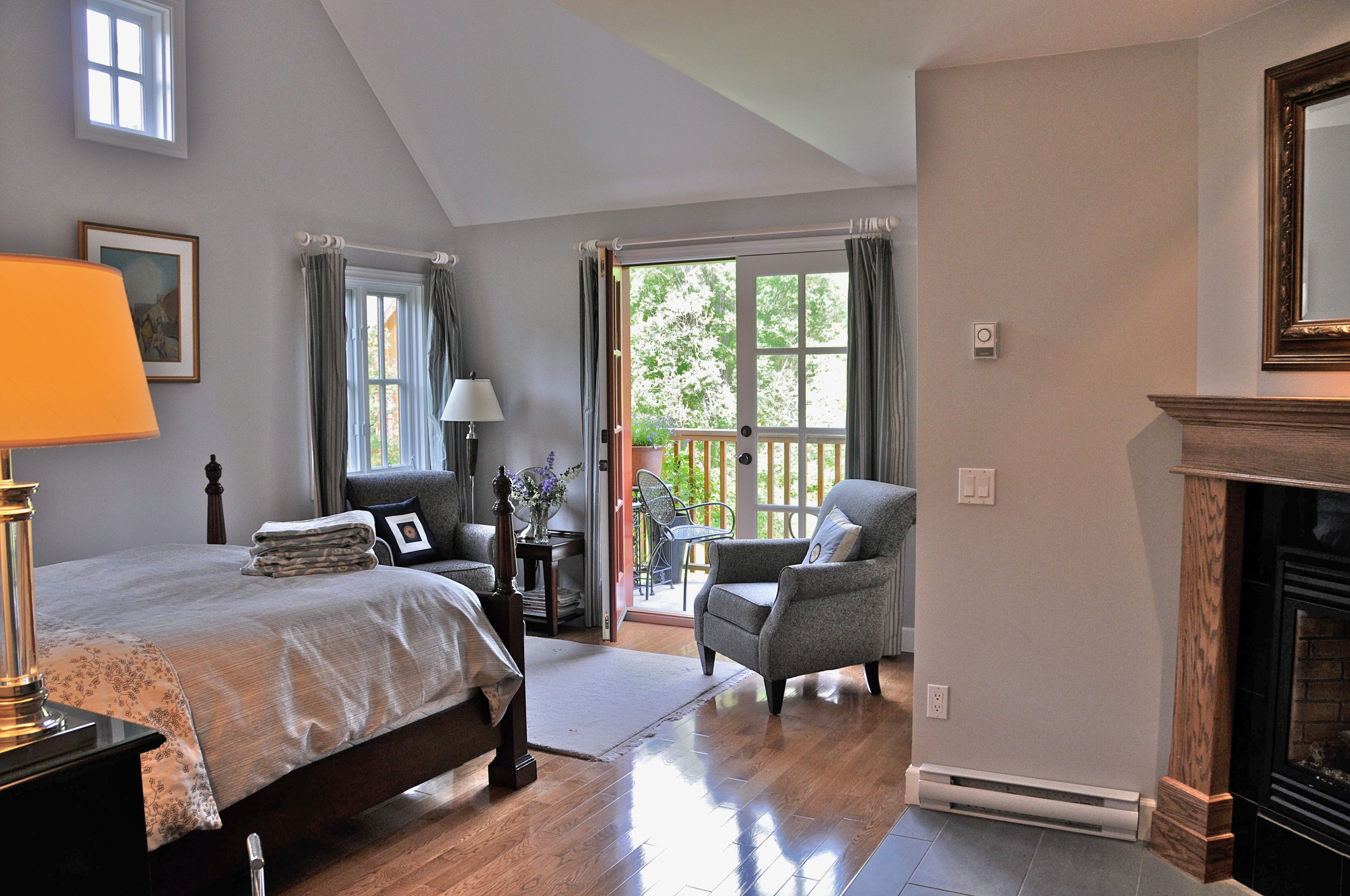 A bedroom with a bed, a chair, a fireplace, and a view of the outdoors.