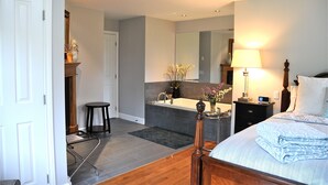 A bedroom with a bed, bedside table, lamp, and a bathroom with a sink and mirror. - Wetherly Inn (Salt Spring Island)