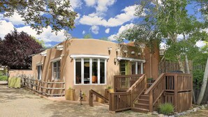 A single-story building with a stucco exterior, a wooden deck, and a staircase leading to a covered porch. - Fully remodeled home in the heart of Historic Santa Fe - AC - Easy stroll to All (Santa Fe)