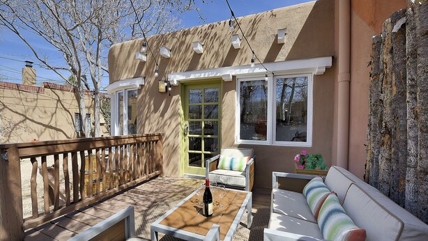 A patio area with a wooden deck, white furniture, and a bottle of wine on a table. - Fully remodeled home in the heart of Historic Santa Fe - AC - Easy stroll to All (Santa Fe)