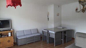 Ein Wohnzimmer mit einer Couch, einem Esstisch, Korbmöbeln, einem Fernseher und einer Chandelier.