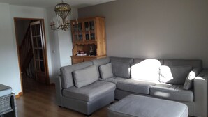 Ein Wohnzimmer mit einem grauen Ecksofa, einer Holzkommode und einer Deckenleuchte.