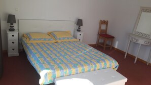 Ein Bett mit gemustertem Überwurf, zwei Nachttische mit Lampen, ein Holzstuhl und eine Kommode mit Spiegel.