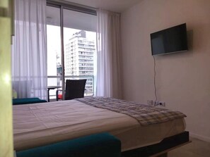 A hotel room with a bed, a chair, a TV, and a balcony with a view of a building. - Independencia 1302 6E by HB (Buenos Aires)