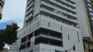 Ein mehrgeschossiges Gebäude mit moderner Architektur, mit Balkonen an jeder Etage und einem im Erdgeschoss befindlichen Gewerbebereich mit Beschilderung.