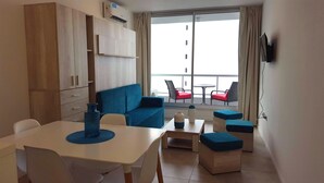 Ein modernes Hotelzimmer mit Essbereich, einem blauen Sofa, einem kleinen Tisch und einem Balkon mit roten Stühlen.