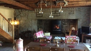 Un interior rústico con chimenea de piedra, vigas de madera en el techo y comedor con manteles florales.