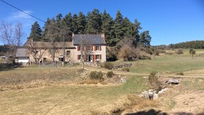 Una casa de piedra con garaje blanco, rodeada por un paisaje rural con árboles y cielo despejado.