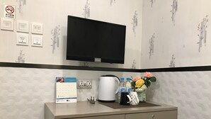 A hotel room with a flat-screen TV mounted above a desk, a calendar, a kettle, and a mini fridge. - Vve Vve Hotel (Kowloon)