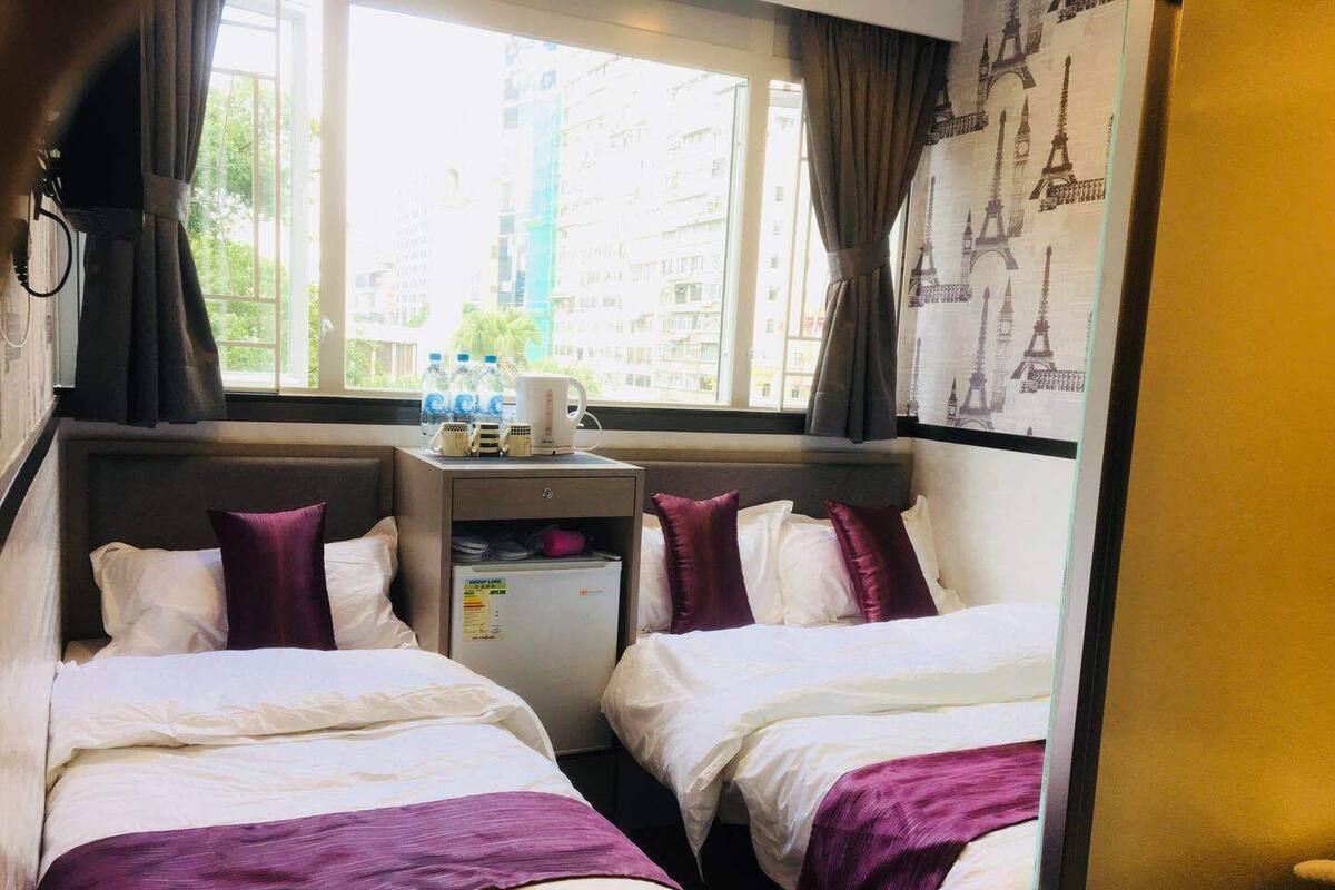 A hotel room with two beds, a small table with a coffee maker, and a window with a view of buildings.