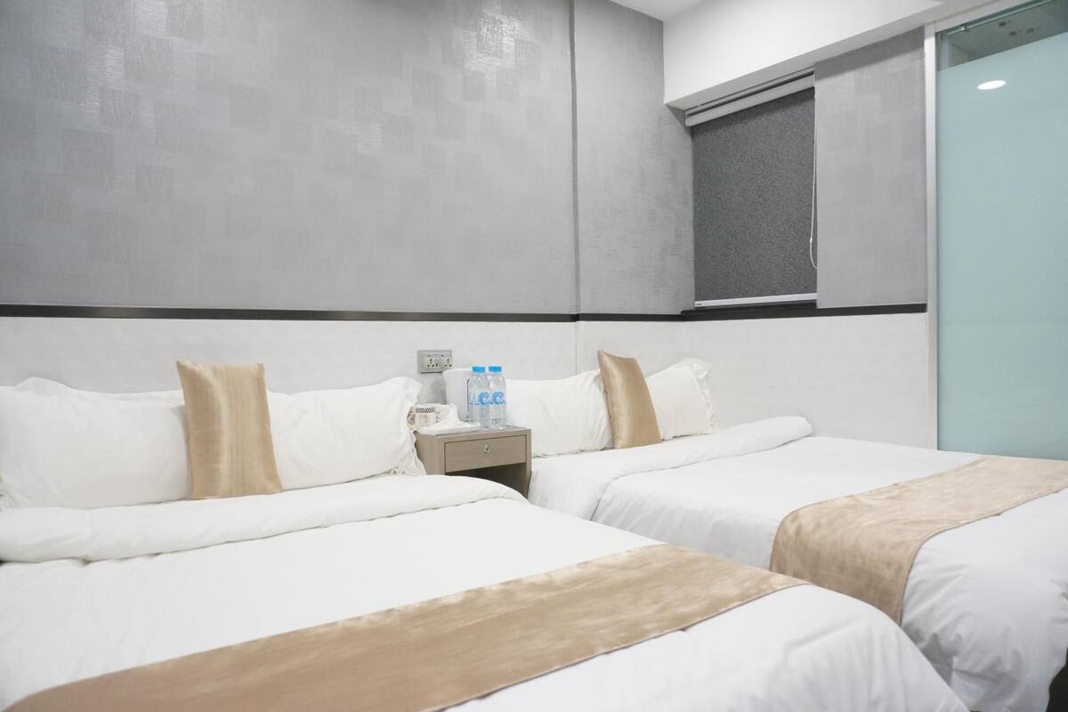 A hotel room with two beds, a nightstand with water bottles, and a window with a view.