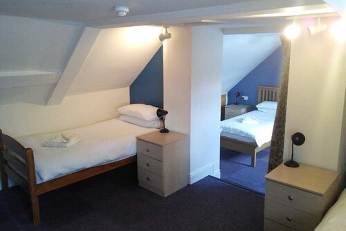 Quarto com uma cama de solteiro, mesa de cabeceira, cômoda e luminária de teto.