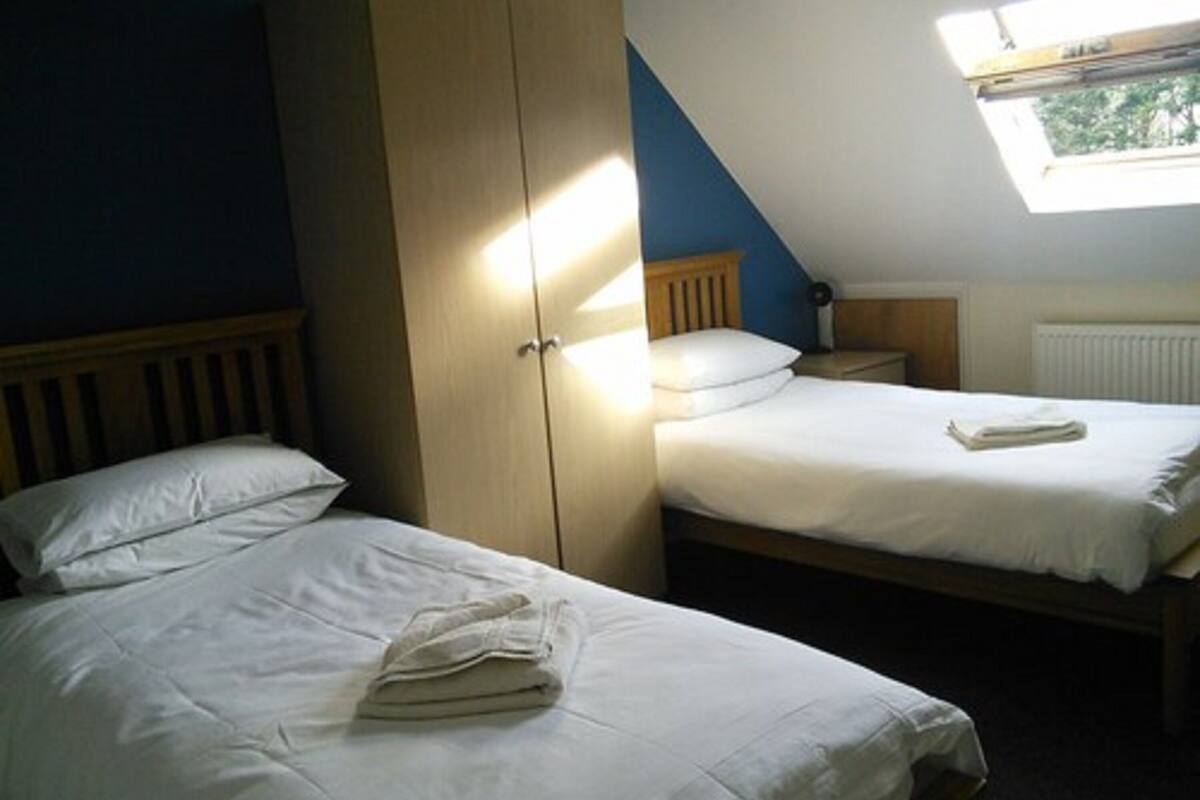 Quarto com duas camas de solteiro, um guarda-roupa, uma janela e um radiador.