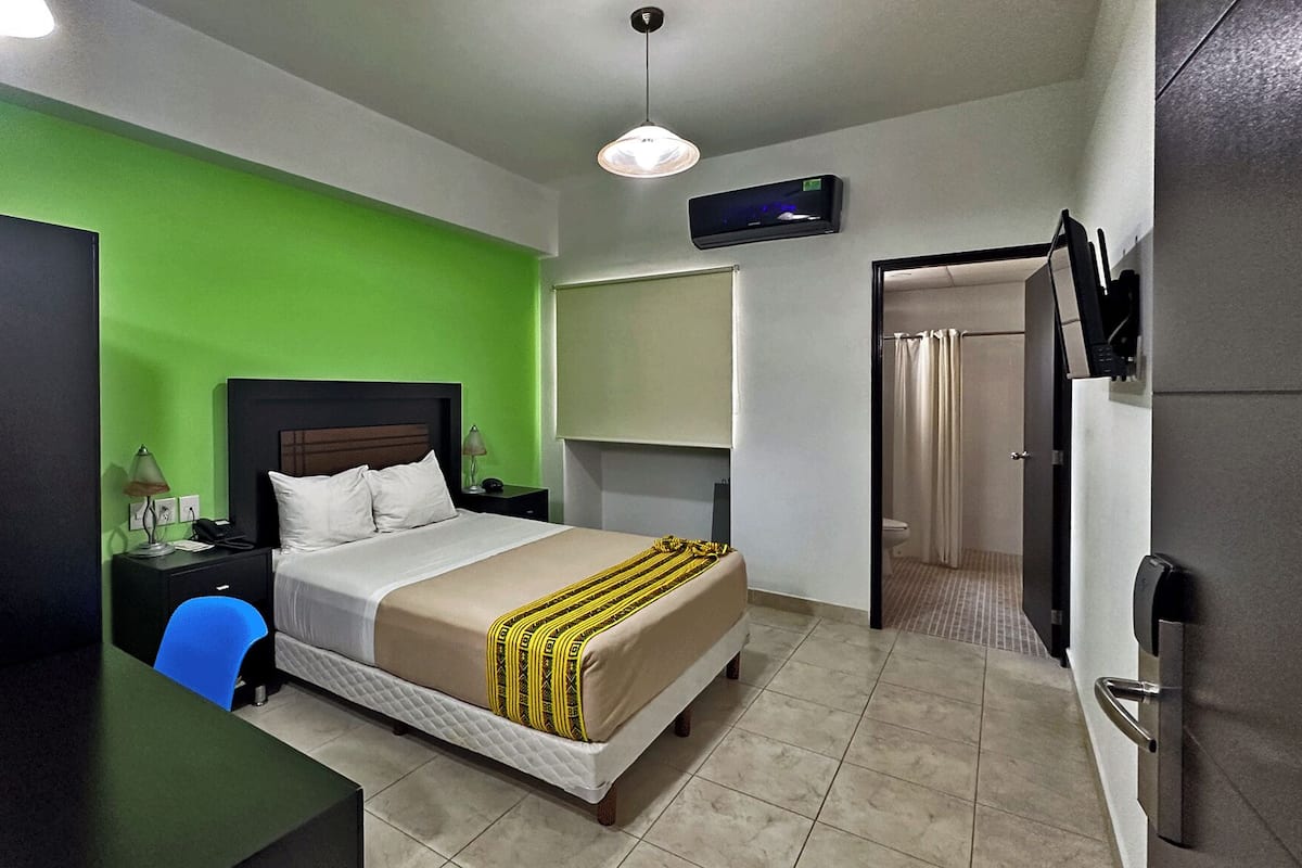 A hotel room with a bed, a desk, a chair, a TV, and a bathroom door.