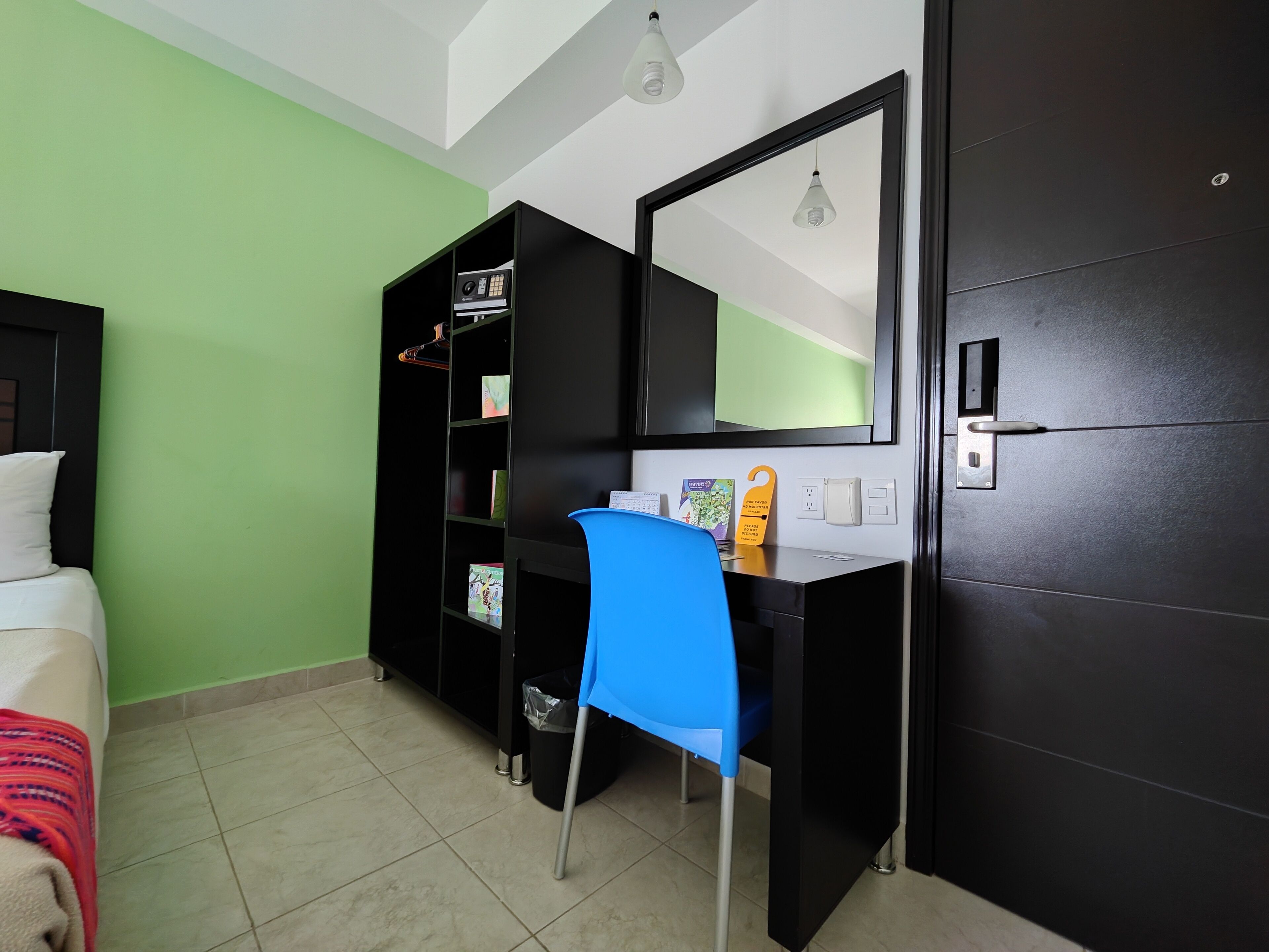 Camera d'albergo con un letto, una scrivania con una sedia, una libreria, uno specchio e una porta.