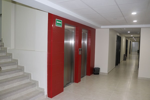 Un pasillo con escalera a la izquierda, paredes rojas y dos ascensores.