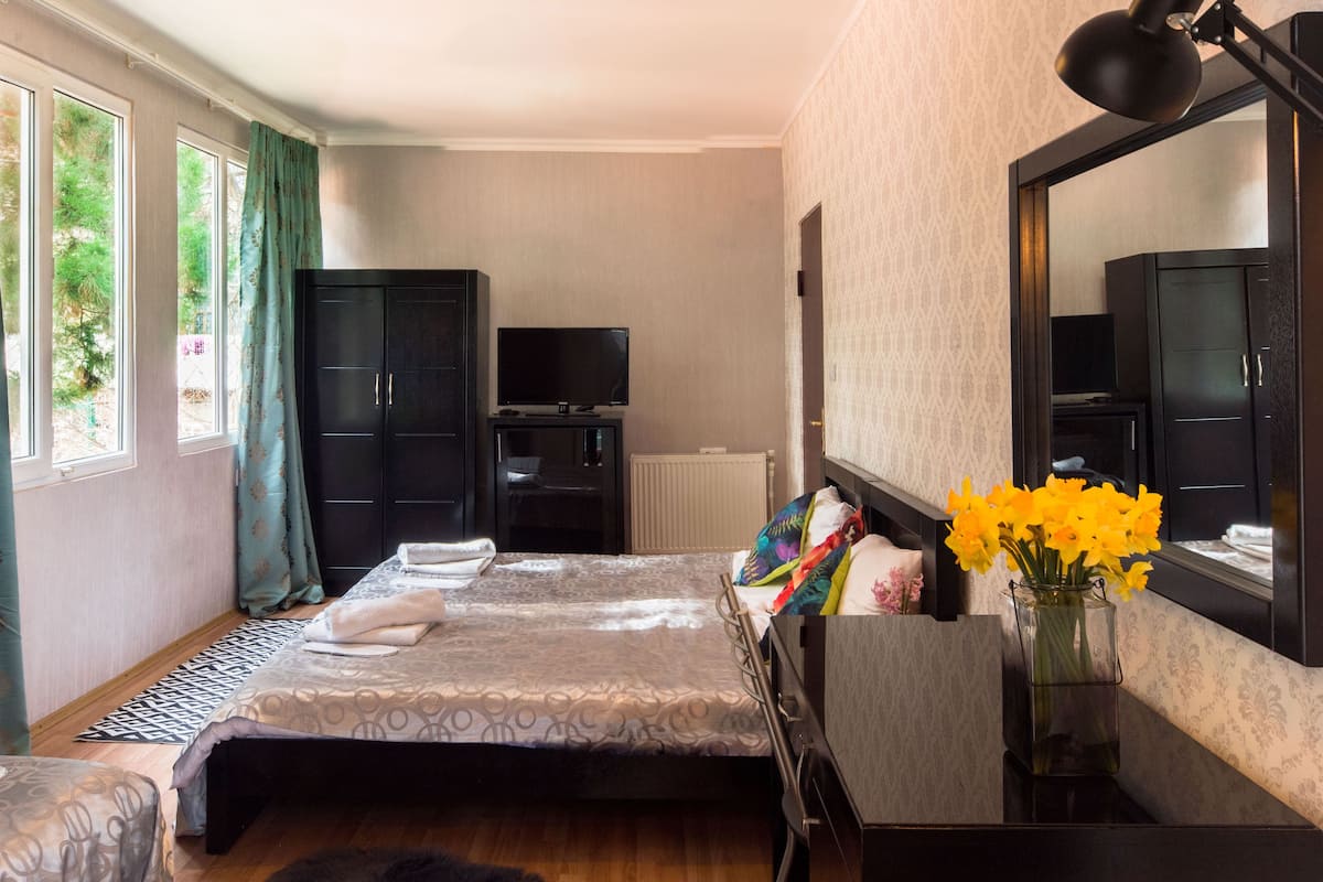 A bedroom with a bed, a dresser, a TV, and a window with curtains.