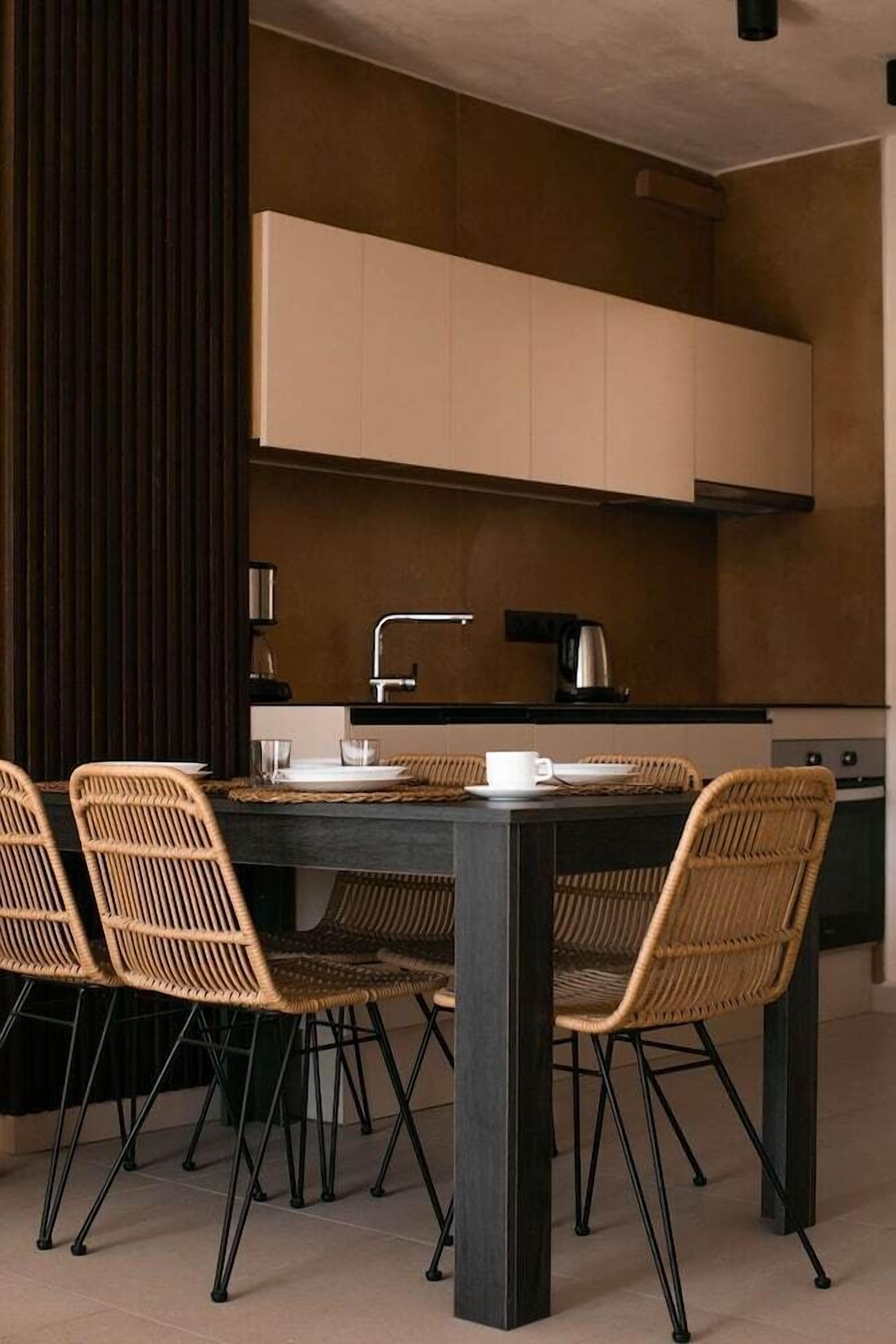Un espace repas moderne avec une table sombre, quatre chaises en osier et une cuisine en arrière-plan.