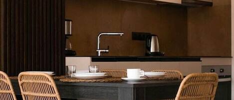 Un espace repas moderne avec une table sombre, quatre chaises en osier et une cuisine en arrière-plan.