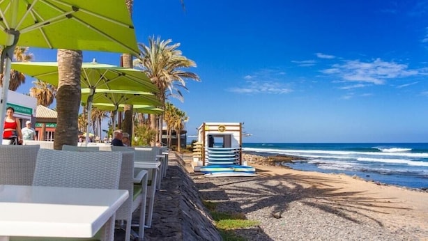 Ein Restaurant direkt am Strand mit Außenbereich, Palmen und Blick auf den Ozean.