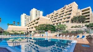 Ein Hotel mit Schwimmbad, mehreren Balkonen und blauem Himmel.