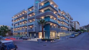 A multi-story hotel with balconies, a central entrance, and a parking area. - Bella Mare (Rethymno)