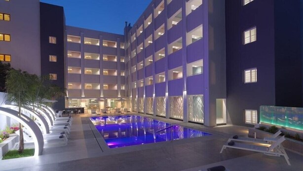 A hotel with a swimming pool, lounge chairs, and a modern architectural design. - Bella Mare (Rethymno)