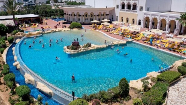 Una gran piscina al aire libre con varias pistas de natación, rodeada de zonas de descanso con sombrillas y tumbonas.