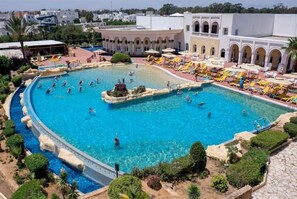 A large outdoor swimming pool with multiple lanes, surrounded by lounge areas with umbrellas and sunbeds. - Medina Belisaire and Thalasso (Hammamet)