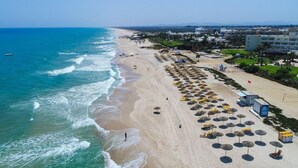 Una playa con sombrillas y sillas reclinables, orilla arenosa y edificios al fondo.