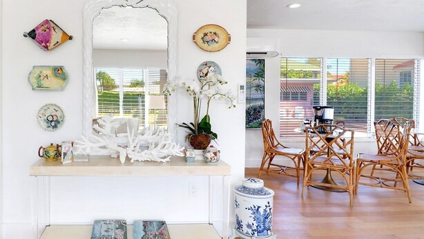 A dining area with a white console table, decorative plates, a vase with white flowers, and wicker chairs. - The Gondolier Inn (Naples)